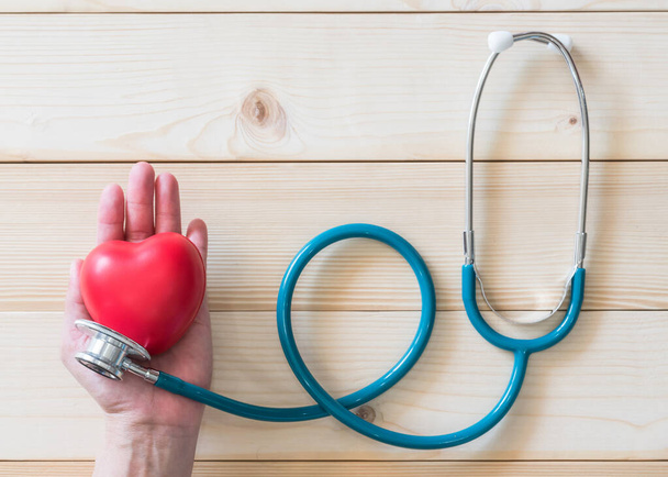 Medyczne ubezpieczenie zdrowotne i koncepcja Światowego Dnia Zdrowia z czerwonym sercem miłości na kobiecej dłoni ze stetoskopem lekarza - Zdjęcie, obraz