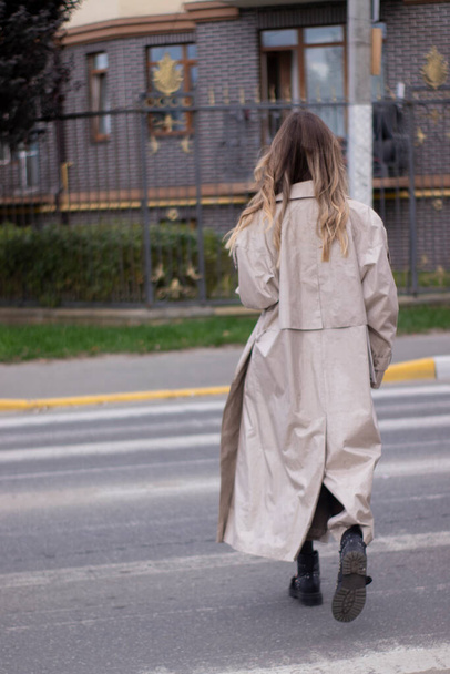 mooi slank jong brunette in modieuze trench jas en zwart jurk kruis een voetgangers kruising - Foto, afbeelding