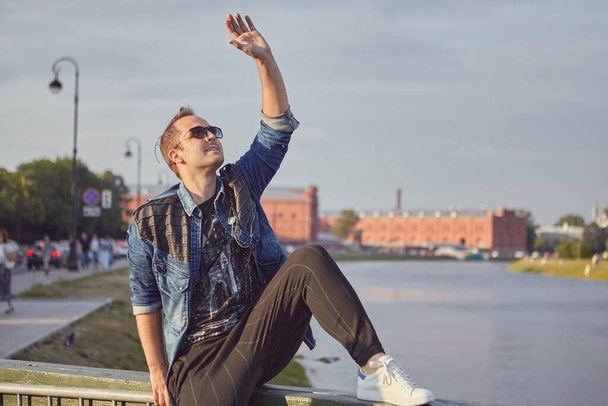 Young white man sits on river bank while travelling. - Valokuva, kuva