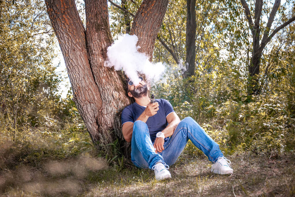 Tarz sahibi bir adam e-sigara içer ve duman bulutu solur. Vape. - Fotoğraf, Görsel