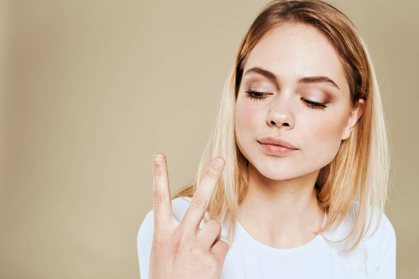 Cheerful blonde woman in a white T-shirt gestures with her hand emotions beige background - 写真・画像