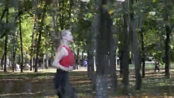 coureuse de fitness caucasienne en tenue de sport courant au parc d'automne le jour ensoleillé - Séquence, vidéo