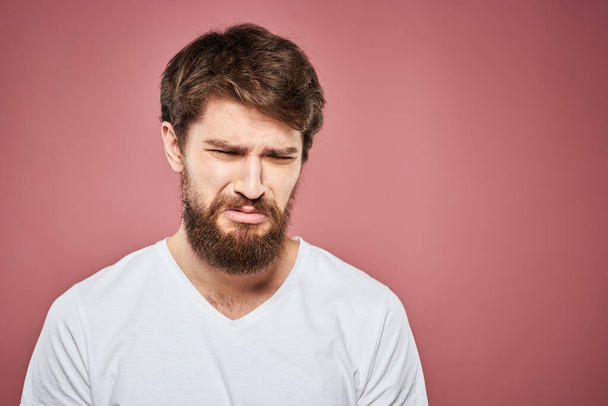 Emotional bearded man in white T-shirt discontent pink background - Foto, Imagen