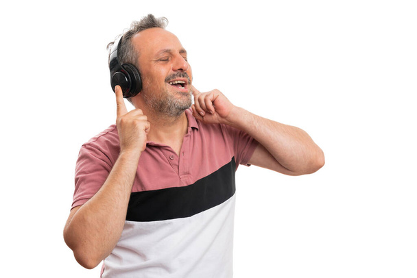 Vidám felnőtt férfi modell mosolyog, ahogy zenét hallgat a fejhallgató énekel tánc viselt színes nyári öltözékben üres copyspace elszigetelt fehér háttér - Fotó, kép