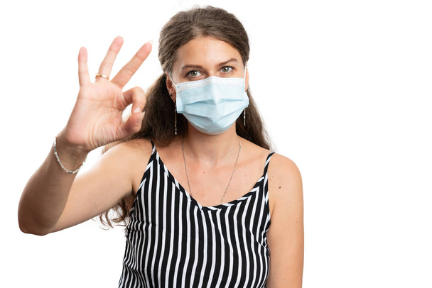 Female model showing okay gesture using fingers wearing disposable medical or surgical mask as prevention for covid19 sars influenza virus contamination in pandemic concept isolated on white - 写真・画像