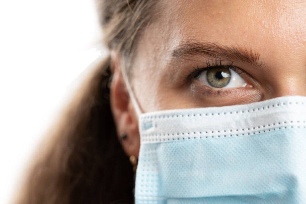 Zbliżenie dorosłej kobiety modelki pół twarzy noszącej medyczną lub chirurgiczną jednorazową maskę jako zakrzepową koncepcję ochrony przed pandemią 19 izolowaną na białym tle - Zdjęcie, obraz