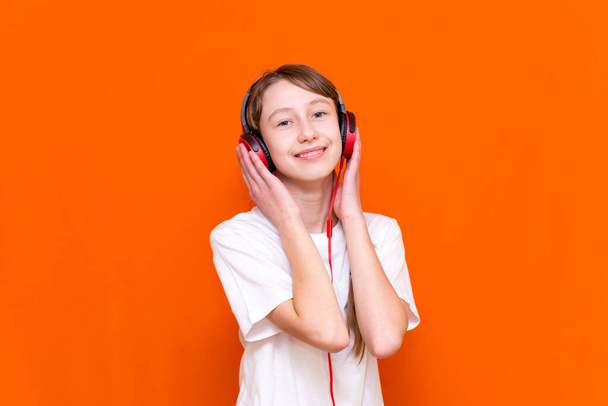 Attractive 12s girl in white t-shirt listens to music on red headphones closeup in a studio indoor - Photo, image