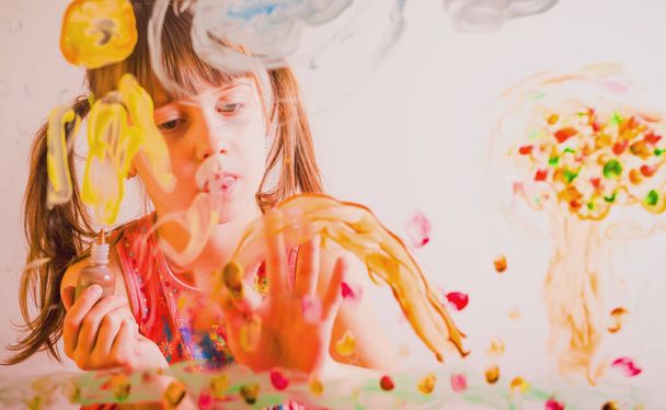 Beautiful young girl painting image on the glass with colorful finger.  - Фото, изображение