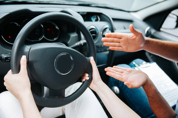 Female hands hold steering wheel. Male instructor demonstrates with his hand what to do with a wheel. Cut close-up view of woman driving a car. Driving courses concept. - Fotó, kép