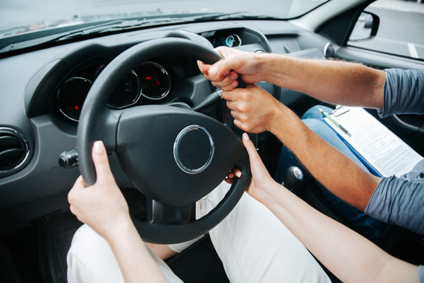 Zwei Hände drehen das Lenkrad zusammen. Fahrschülerin hält das Steuer in der Hand und männlicher Fahrlehrer hilft ihr beim Autofahren. Fahrschulkonzept. Nahsicht. - Foto, Bild