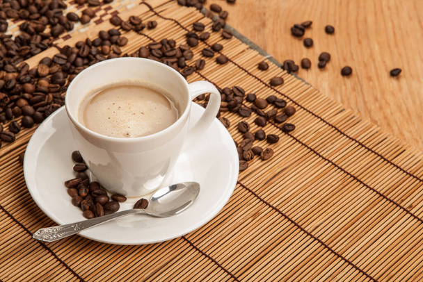taza de café aromático con espuma en una servilleta de bambú con granos de café - Foto, imagen