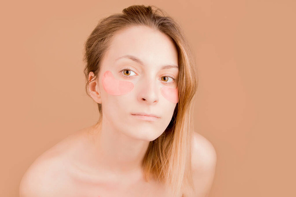 Girl with pink patches under the eyes on a beige background. - Photo, Image
