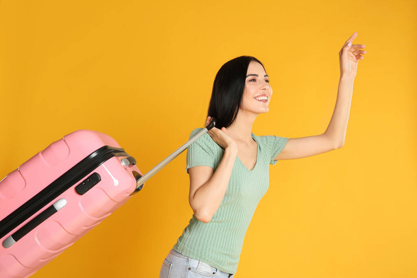 Beautiful woman with suitcase for summer trip on yellow background. Vacation travel - Фото, изображение