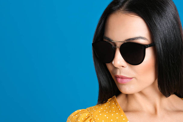 Beautiful woman wearing sunglasses on blue background, closeup. Space for text - Fotó, kép