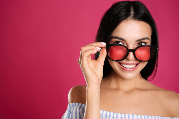 Beautiful woman wearing sunglasses on pink background, closeup. Space for text - 写真・画像