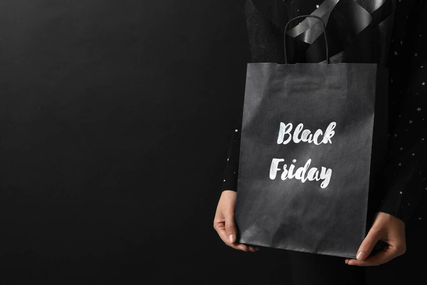 Woman holding shopping bag with words Black Friday on dark background, closeup. Space for text - Foto, afbeelding