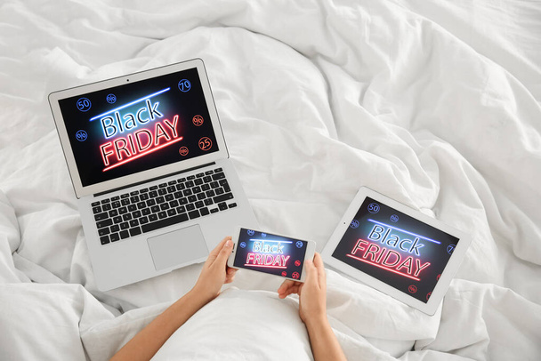 Woman using tablet, mobile phone and laptop with Black Friday announcement in bed, above view - Foto, immagini