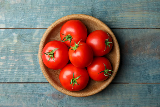 Ripe tomatoes in bowl on blue wooden table, top view - Foto, Imagen