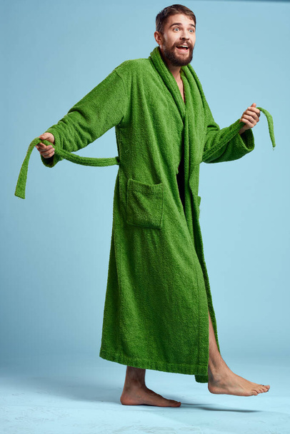 a man in a green robe in full growth on a blue background barefoot - Фото, изображение