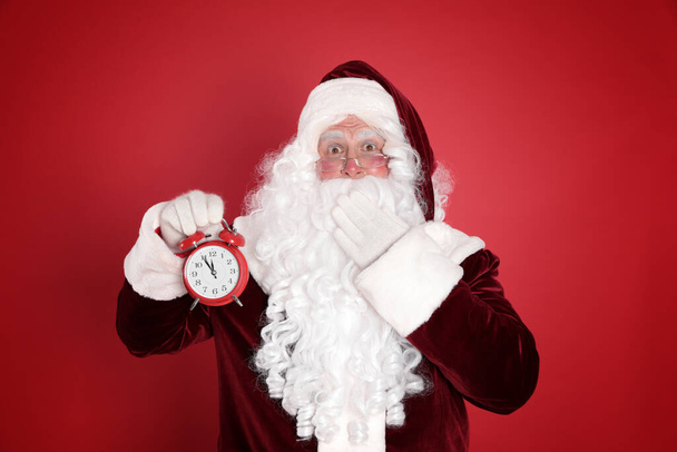 Santa Claus holding alarm clock on red background. Christmas countdown - Foto, imagen