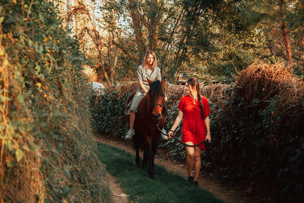 Két barátnő cseveg és lovagol a lovával a vidéken. - Fotó, kép