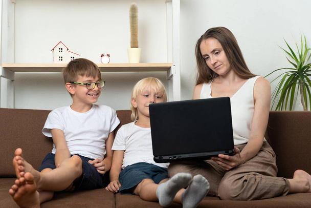 Anya két fiával a laptop képernyőjét nézi. Házit csinálok gyerekekkel. Otthoni oktatás. - Fotó, kép