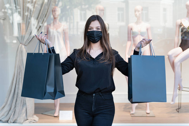 Stílusos nő fekete ruhában és védő maszk tartja fekete bevásárló táskák. Bemutató háttér. Mockup. Fekete péntek koncepció. - Fotó, kép
