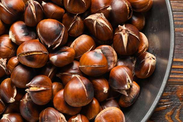 Delicious roasted edible chestnuts in frying pan on wooden table, top view - Φωτογραφία, εικόνα