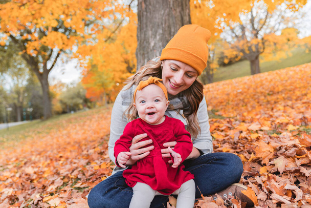 Baby daughter and her mother in the autumn season in park - Photo, Image