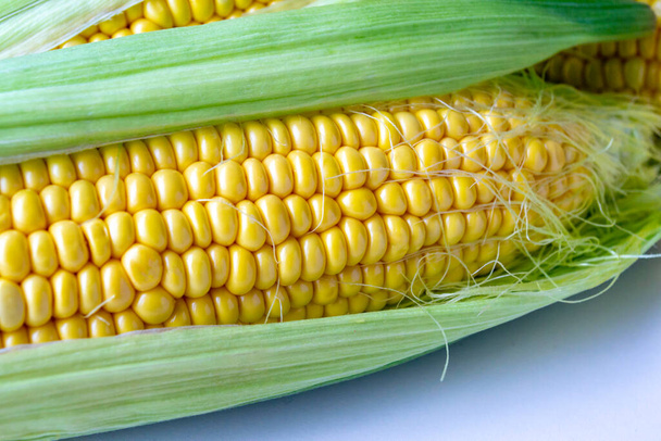 Ucho kukurydzy leży na stole. Świeża kukurydza z liśćmi. Zamknij się. - Zdjęcie, obraz