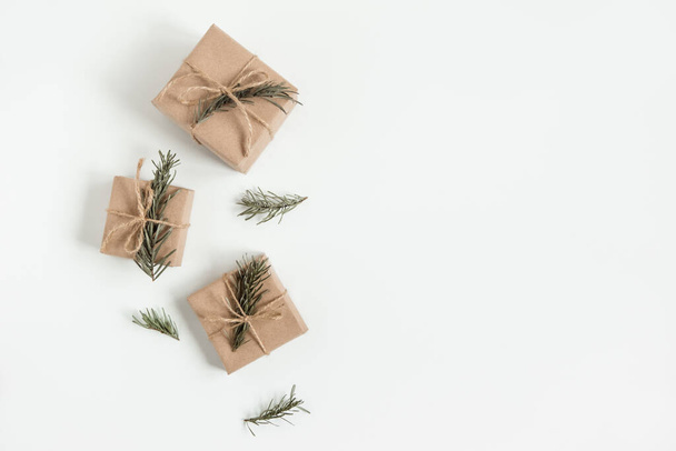 Composición plana de Navidad de cajas de regalo artesanales con ramas de abeto sobre el fondo blanco. Caja de papel marrón hecha a mano con rama de árbol de Navidad. Copiar espacio - Foto, imagen