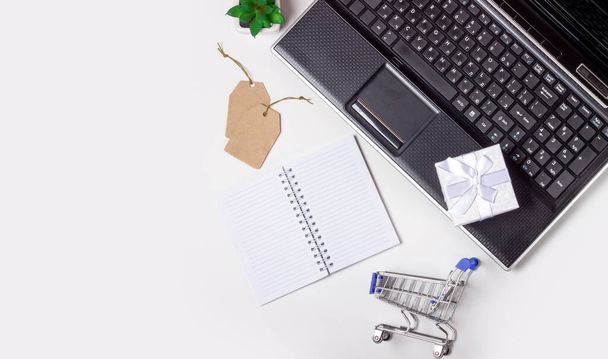 Laptop, note book and shopping trolley on a white background. Online shopping concept - Фото, изображение