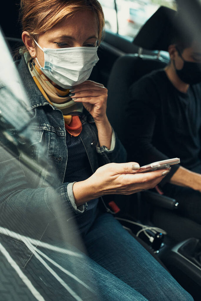 Woman talking on phone using smartphone sitting in a car wearing the face mask to avoid virus infection and to prevent the spread of disease in time of coronavirus - Foto, afbeelding