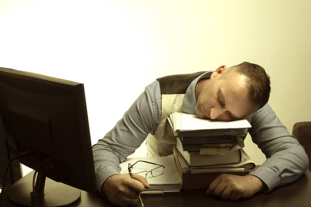 Un uomo dorme sul posto di lavoro su un mucchio di carta. Ufficio lavoratore dorme sul tavolo - Foto, immagini