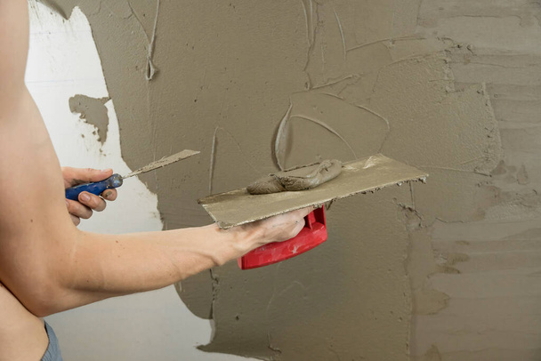 Un trabajador enlustra la pared con una espátula y aplica una solución de mezcla de cemento. El reparador coloca el yeso en los paneles de yeso. Handyman repara su casa. El trabajador restaura la vivienda. Especialista encubre grietas - Foto, Imagen