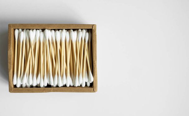 Eco-friendly cotton swabs. A cardboard box containing recyclable bamboo cotton buds on a gray surface. Zero waste concept. Eco product. Cosmetic sticks in a box. Wooden sticks for cleaning ears. - 写真・画像