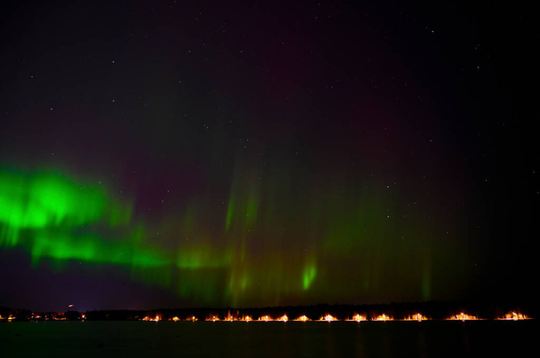 Ein Landschaftsbild von Aurora borealis grüner Strahl von Nordlichtern mit violettem Schweif neben einem See unter Sternenhimmel mit Reflexion in skandinavischem Land - Foto, Bild