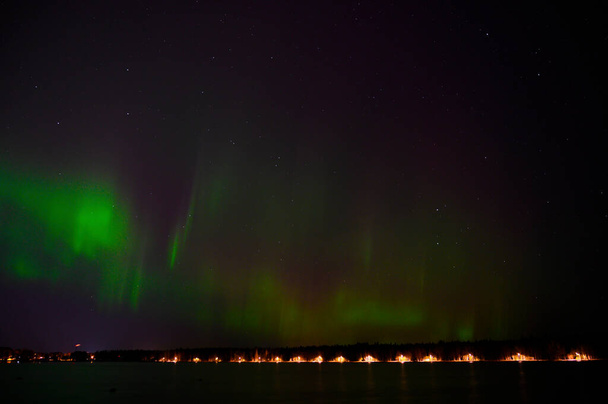 Nightscape view of Aurora borealis green beam of northern lights with purple хвост рядом с озером под звездным небом с видом на скандальную страну - Фото, изображение
