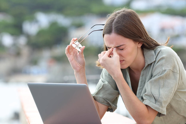 Stressed woman using laptop suffering eyestrain complaining outdoors in a balcony - Foto, imagen