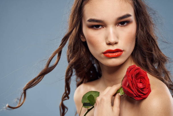 Portret kobiety z czerwoną różą w pobliżu twarzy na szarym tle i makijaż kręcone włosy - Zdjęcie, obraz