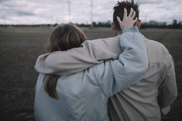 una pareja enamorada camina en un campo de soja abierto por la noche en clima nublado y abraza mucho - Foto, imagen