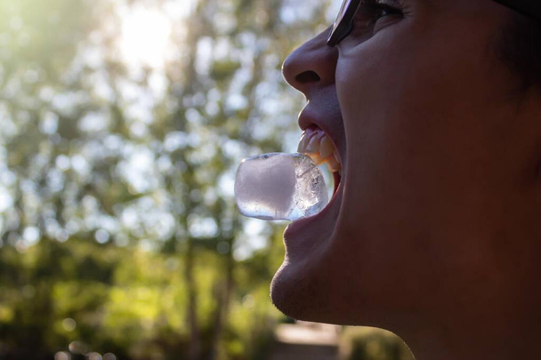 giovane uomo che tiene un cubetto di ghiaccio tra i denti in una giornata estiva - Foto, immagini