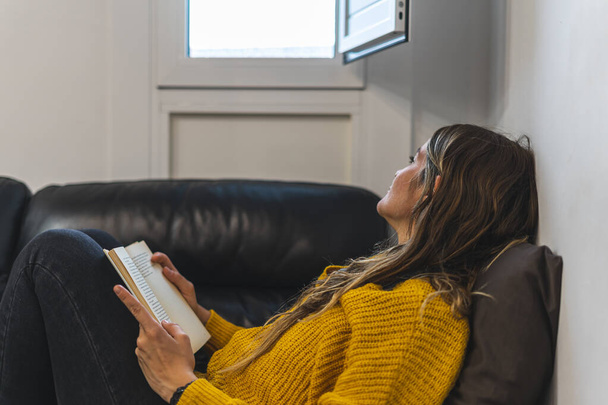 Jeune femme lisant sur le canapé devant la fenêtre - Photo, image