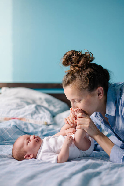 A young mom is kissing a newborn. Motherhood is the happiness of motherhood. New life of the infant at home. Caring feelings love tenderness. The mother admires the child. Happy cute woman and son - Фото, зображення