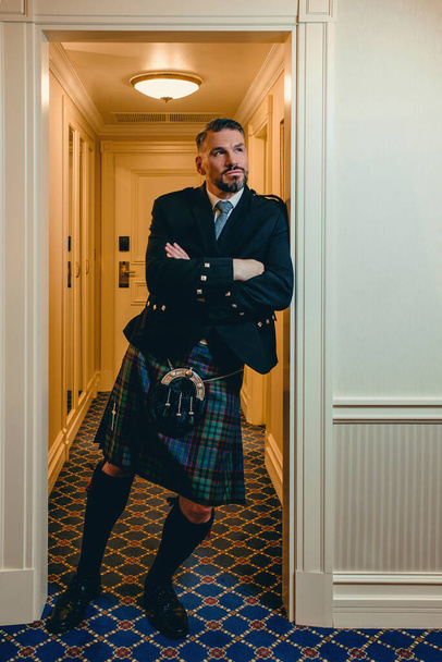 guapo maduro valiente elegante hombre (gay) escocés en kilt en habitación de hotel de lujo. Estilo, moda, estilo de vida, cultura, viajes, concepto étnico. - Foto, Imagen