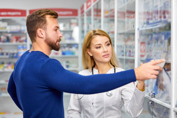 male customer having a discrete talk with druggist in pharmacy - Foto, Imagen