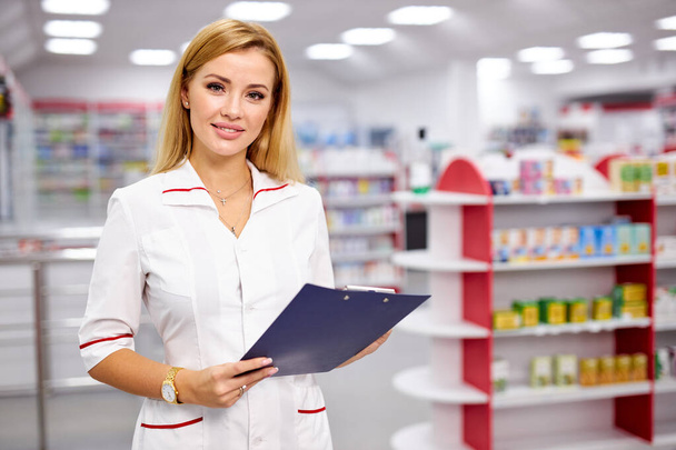 pleasant female pharmacist writing on clipboard at pharmacy, make notes - Foto, imagen