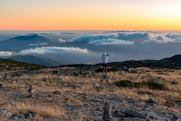Puesta de sol en la cima del Parque Natural de la Serra da Estrela, Portugal con nubes bajas y una persona observando el paisaje con su cámara - Foto, imagen