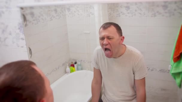Junger Mann wird krank, untersucht seine Zunge im Spiegel, berührt seine Stirn - Filmmaterial, Video
