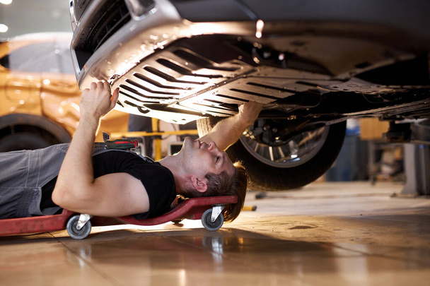 side view on concentrated auto mechanic male working alone on the floor - Foto, afbeelding